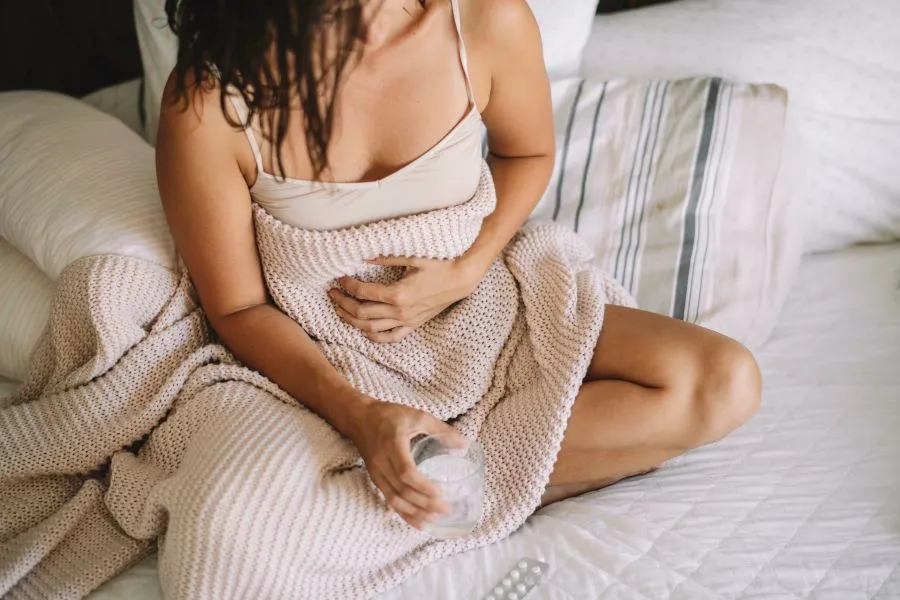 A woman sitting in bed holding her stomach and holding a glass of water.